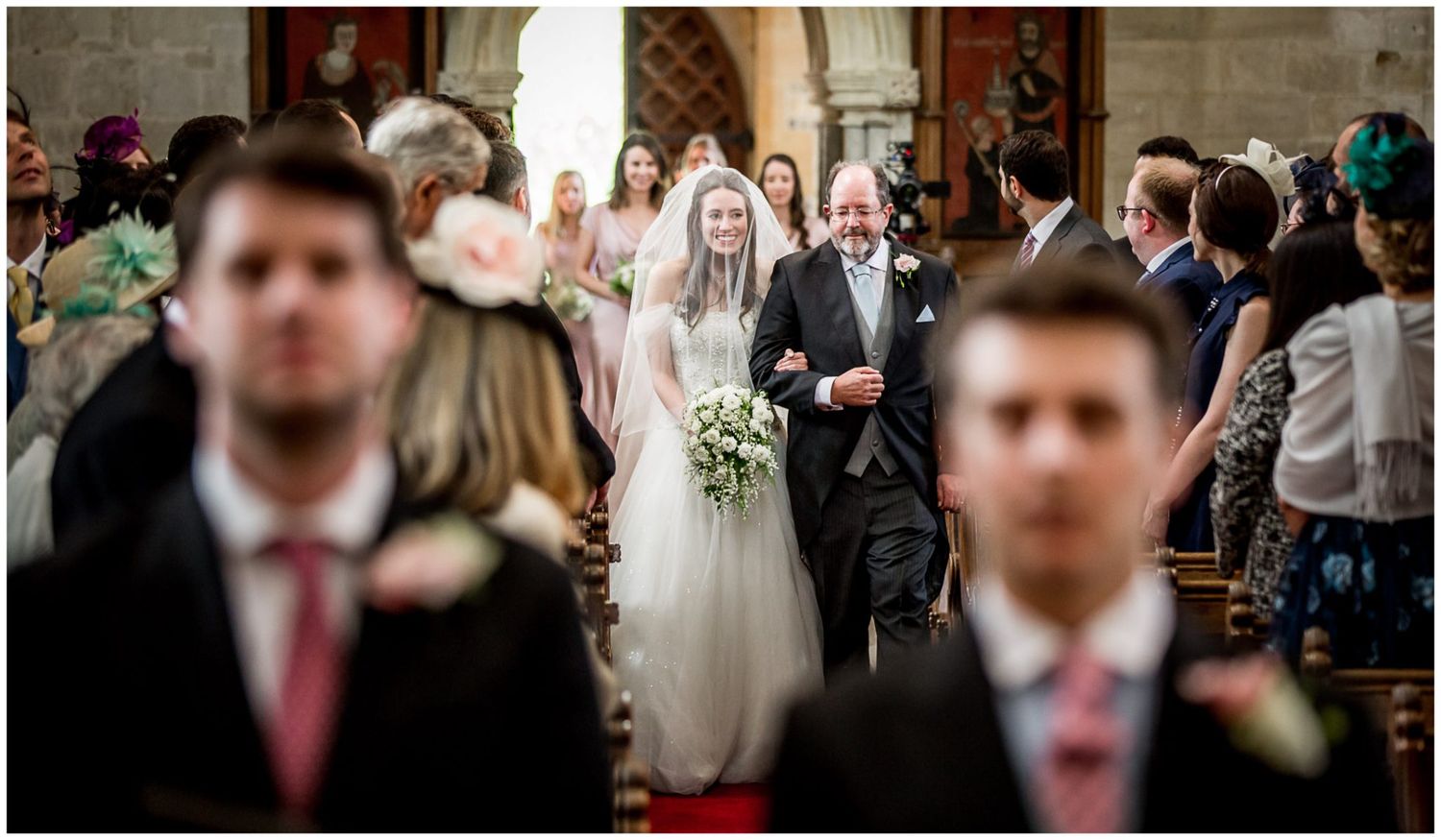 Wedding guests gather inside a historic church with wooden pews and ornate architectural details.