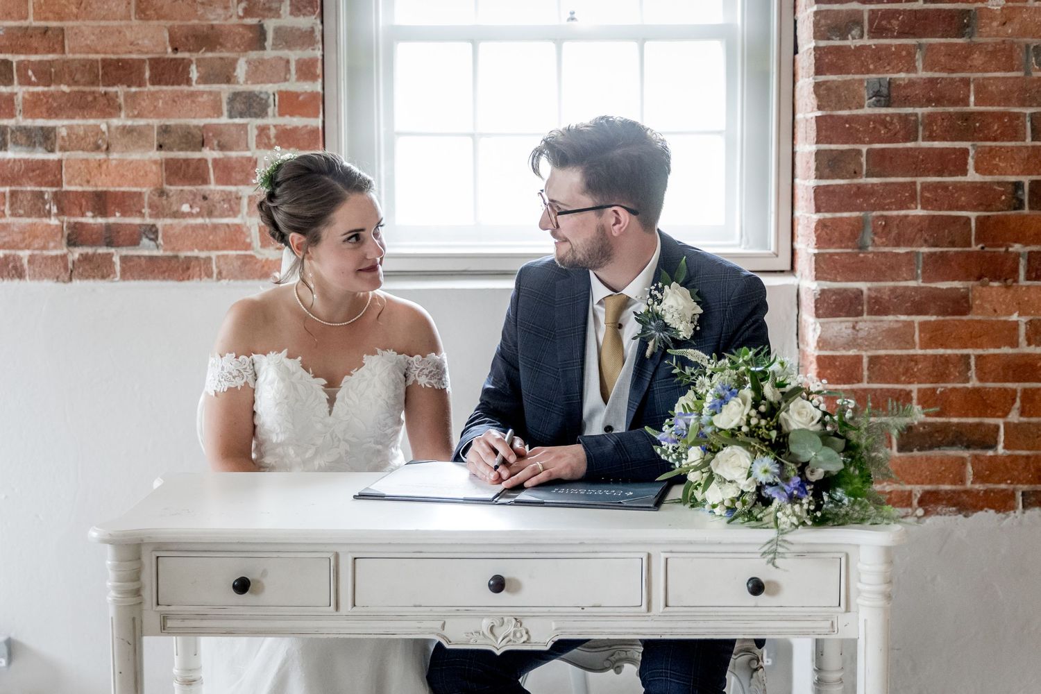 Document signing moment during wedding ceremony in bright brick-walled room.