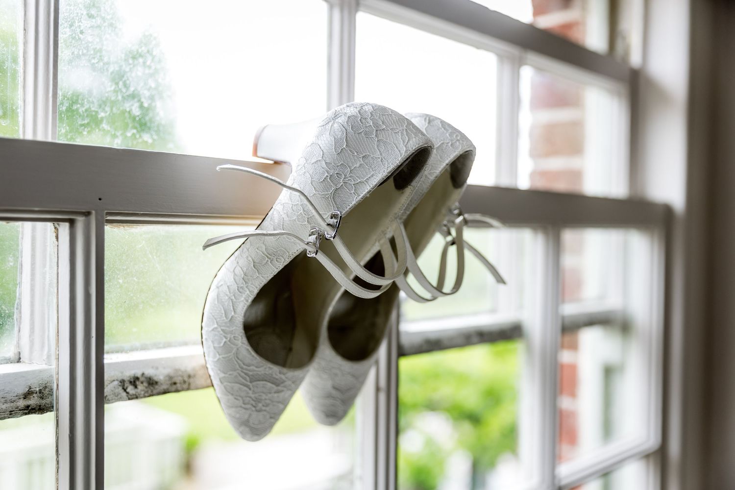 Wedding shoes displayed on windowsill with natural light streaming in.