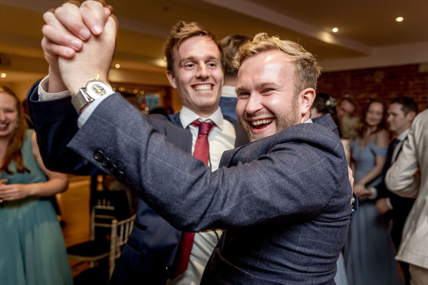 Wedding guests dancing and laughing together during an indoor celebration.