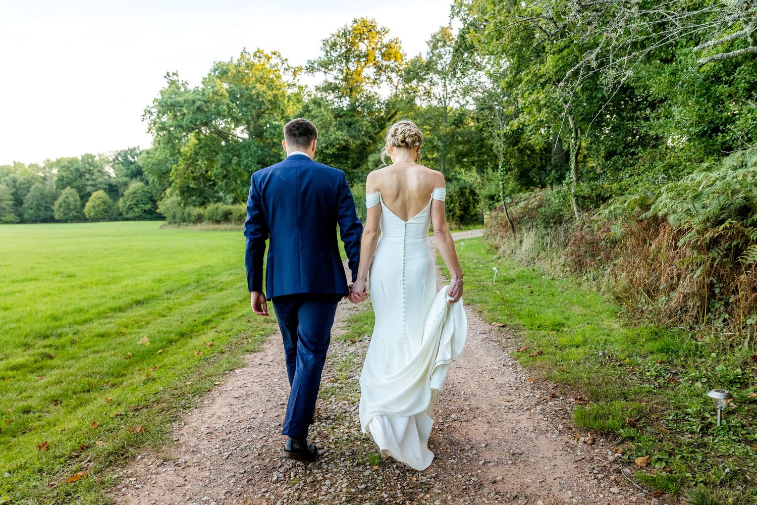 A couple walks along a scenic country path surrounded by lush green trees and grass.