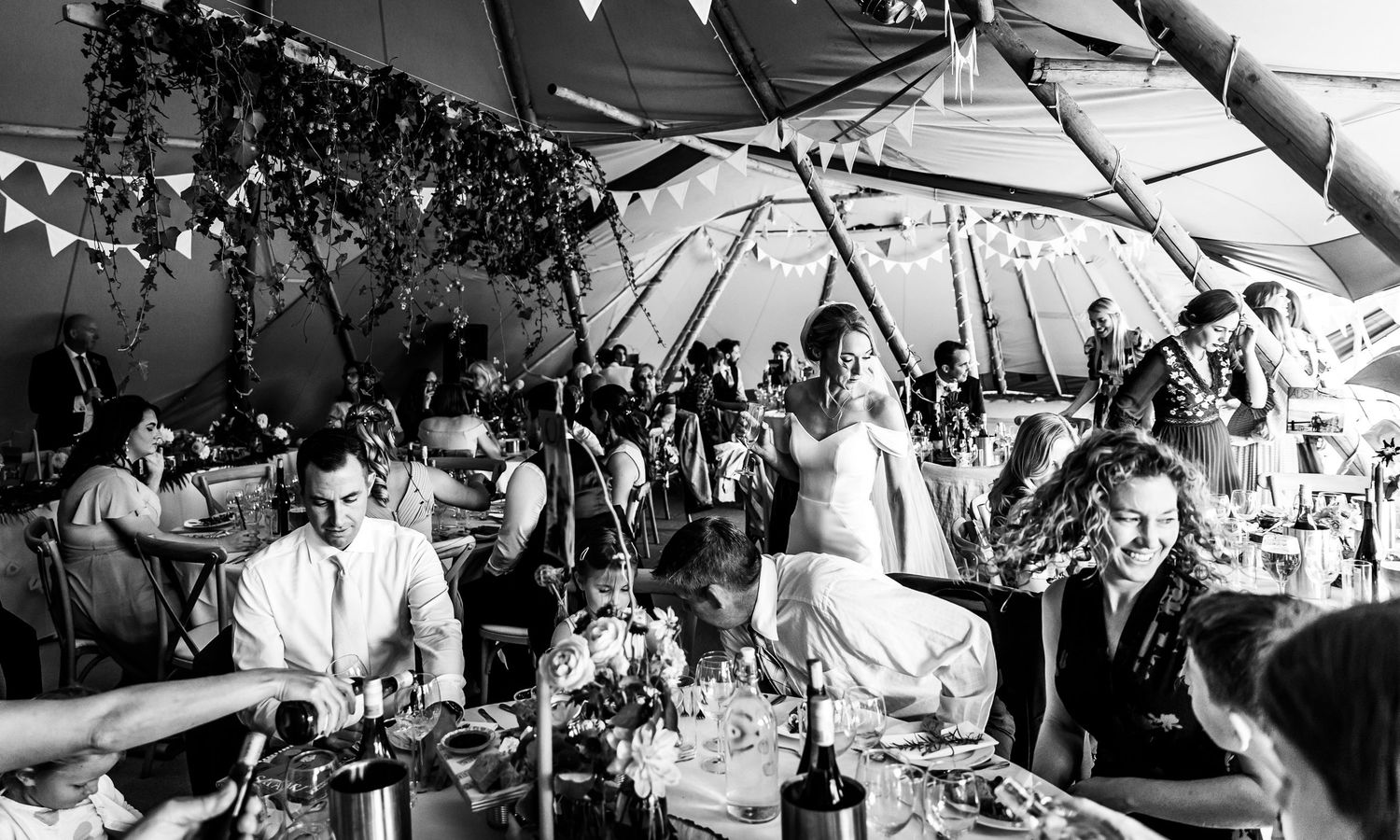 Black and white photo of wedding guests dining under a tent with festive bunting decorations.