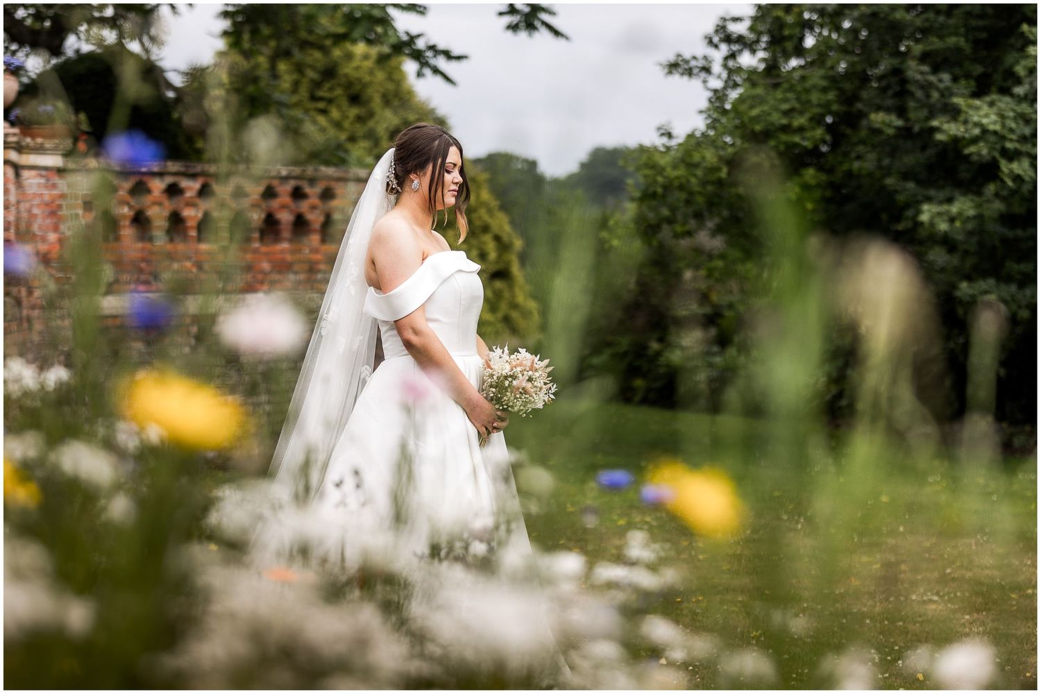 Bride in white wedding dress holding bouquet poses among wildflowers in the gardens at The Elvetham wedding hotel in Hampshire