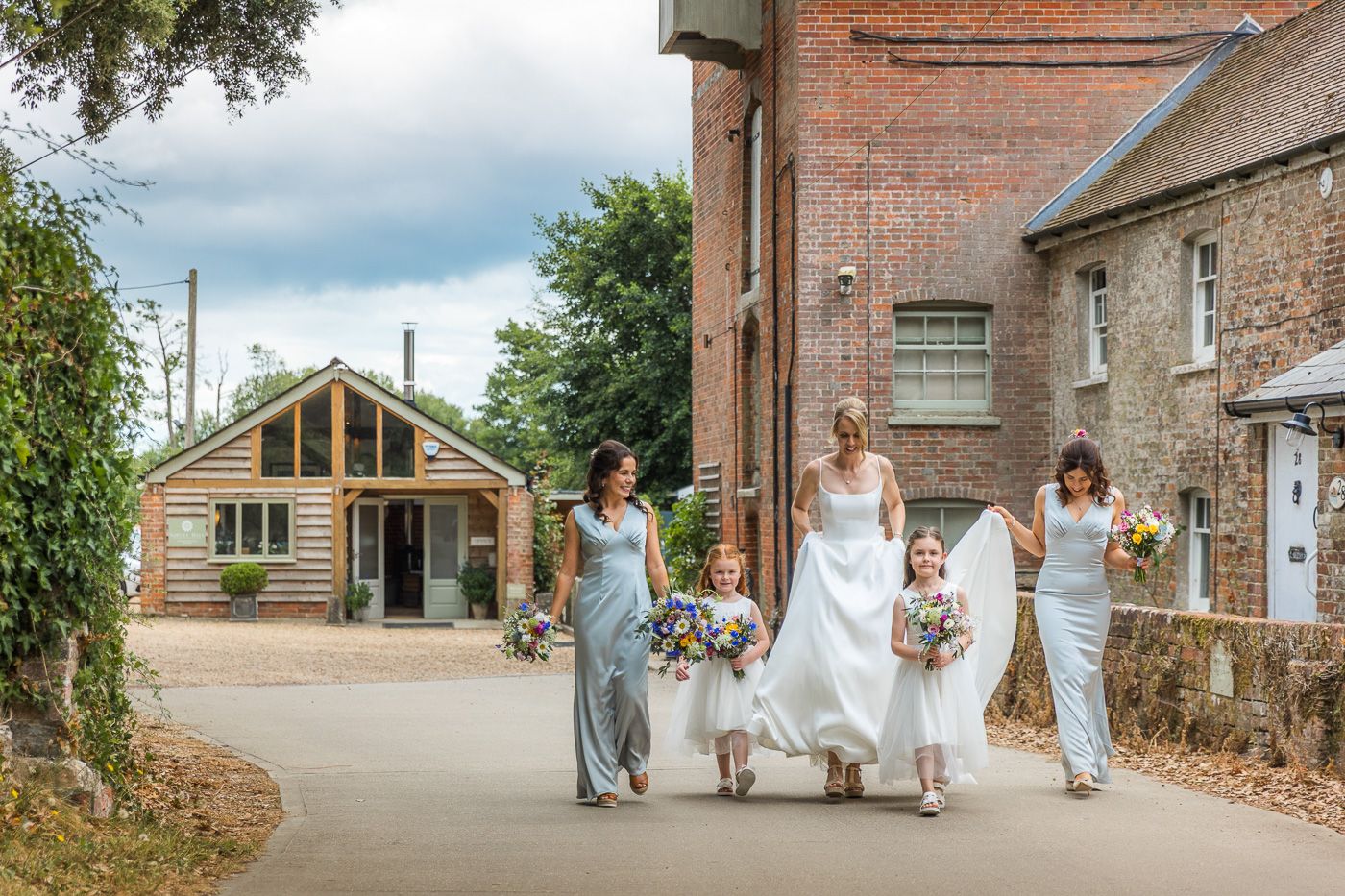 Wedding party in coordinated dresses walking together down rustic village street.