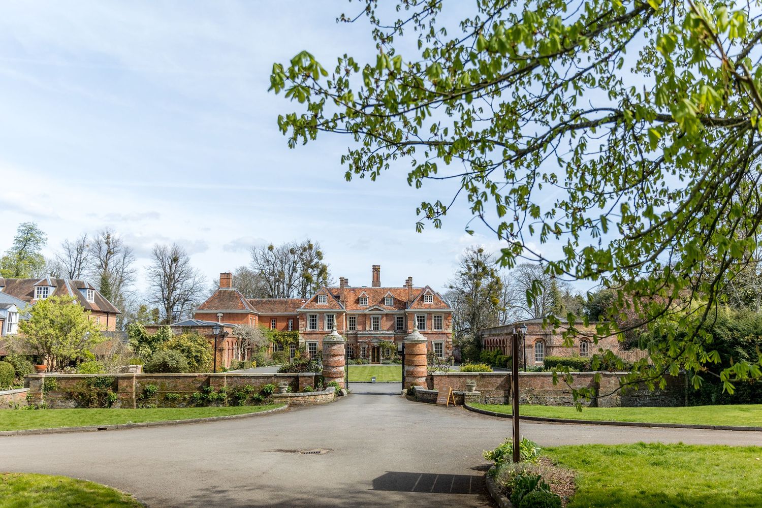 Grand country estate with manicured grounds and entrance driveway on sunny day.