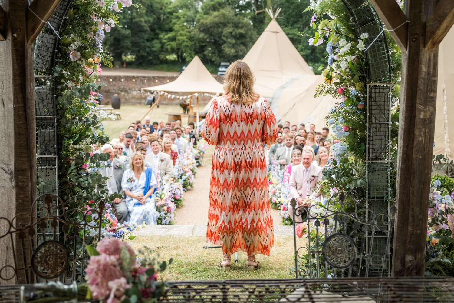 Rustic outdoor wedding venue with wooden beams and tipi tents in the background.