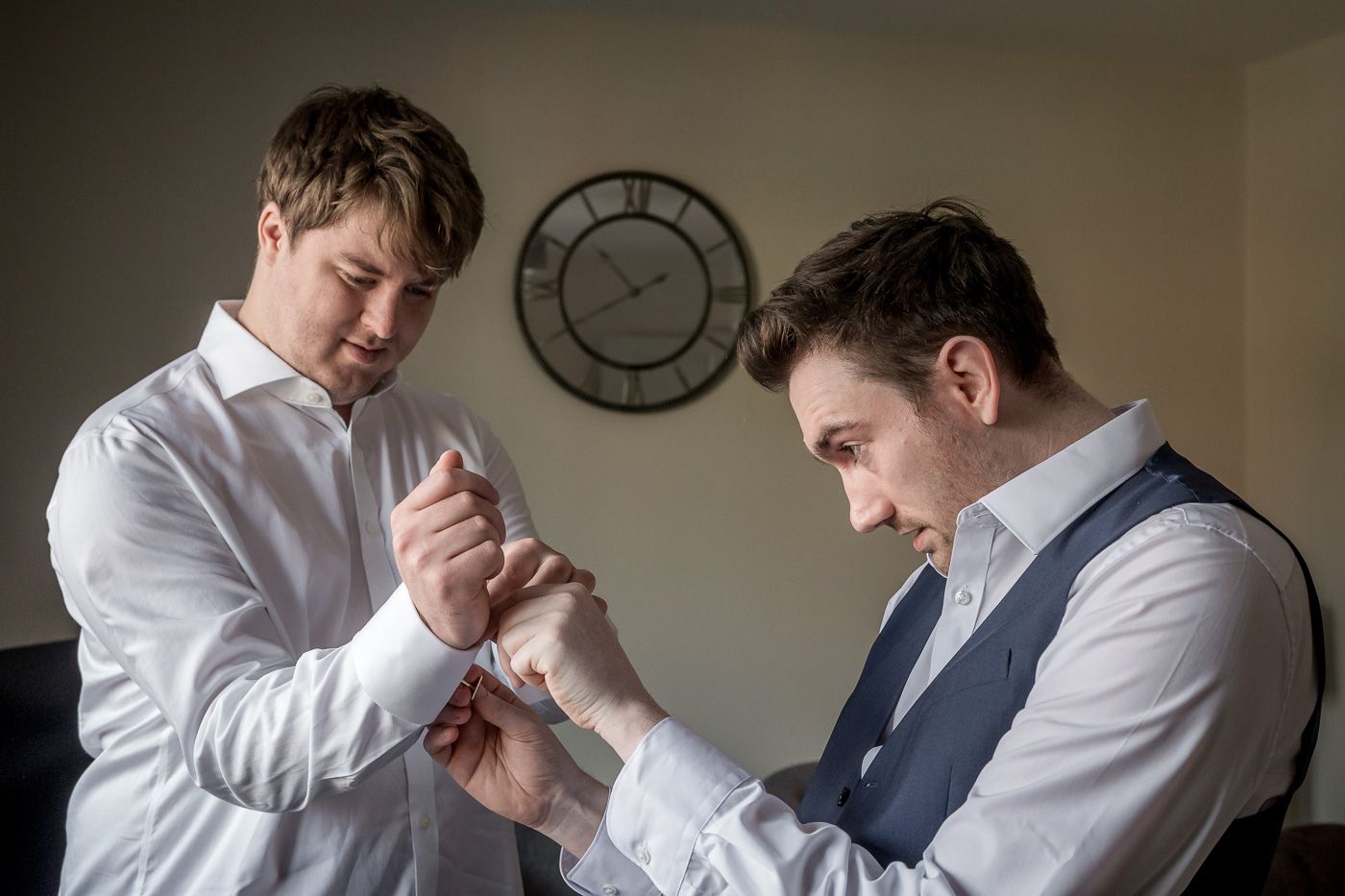 Men helping each other with cufflinks and suit preparations before the ceremony.