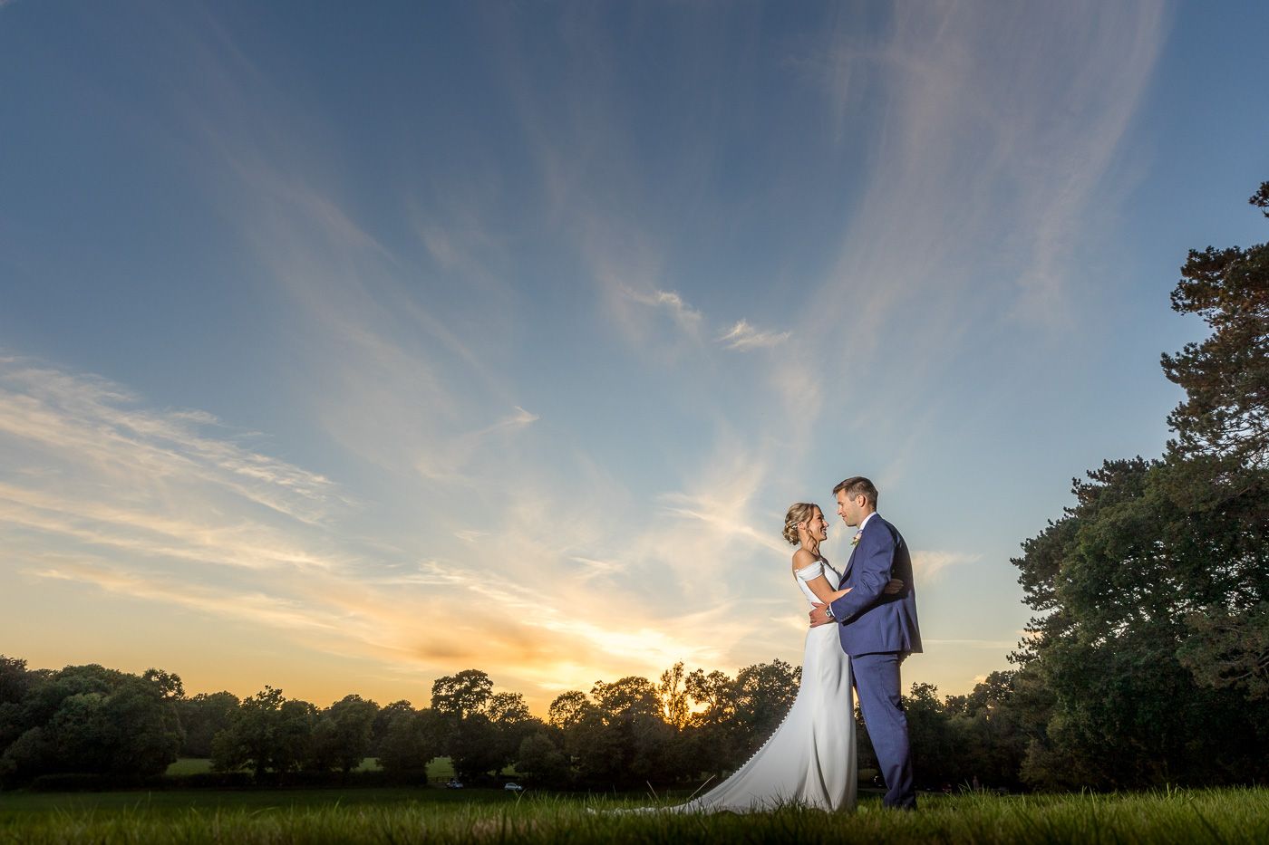 A couple embraces during golden hour sunset for their wedding portrait in a field.