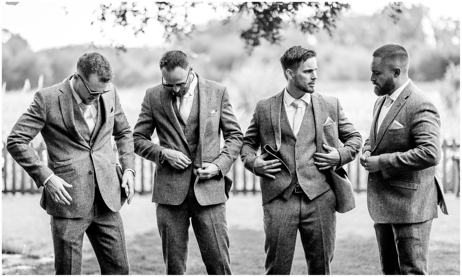 Groomsmen in gray suits sharing a candid moment at outdoor wedding.