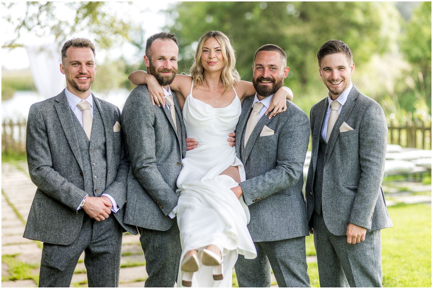 Wedding party in grey suits and white dress pose together on grass.