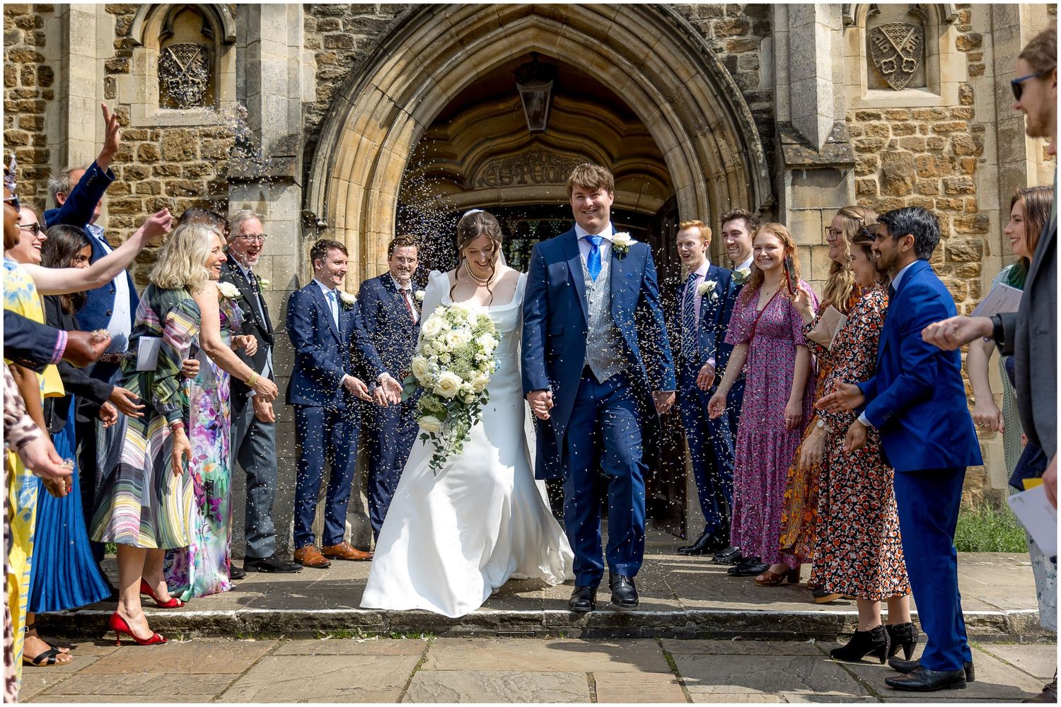 Wedding celebration under stone archway with guests lined up along church entrance.