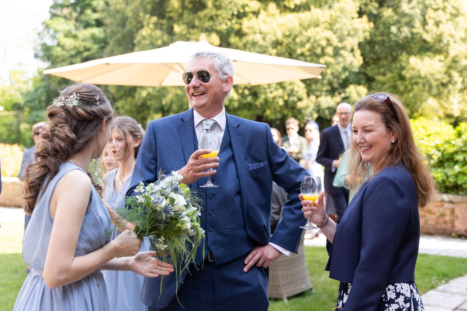 Wedding guests enjoying champagne and conversation in a sunny garden setting.