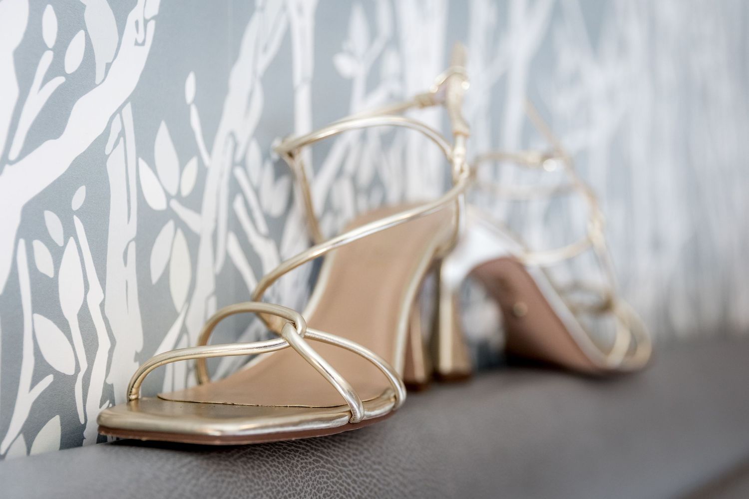 Elegant strappy wedding heels in cream color against textured wallpaper background.