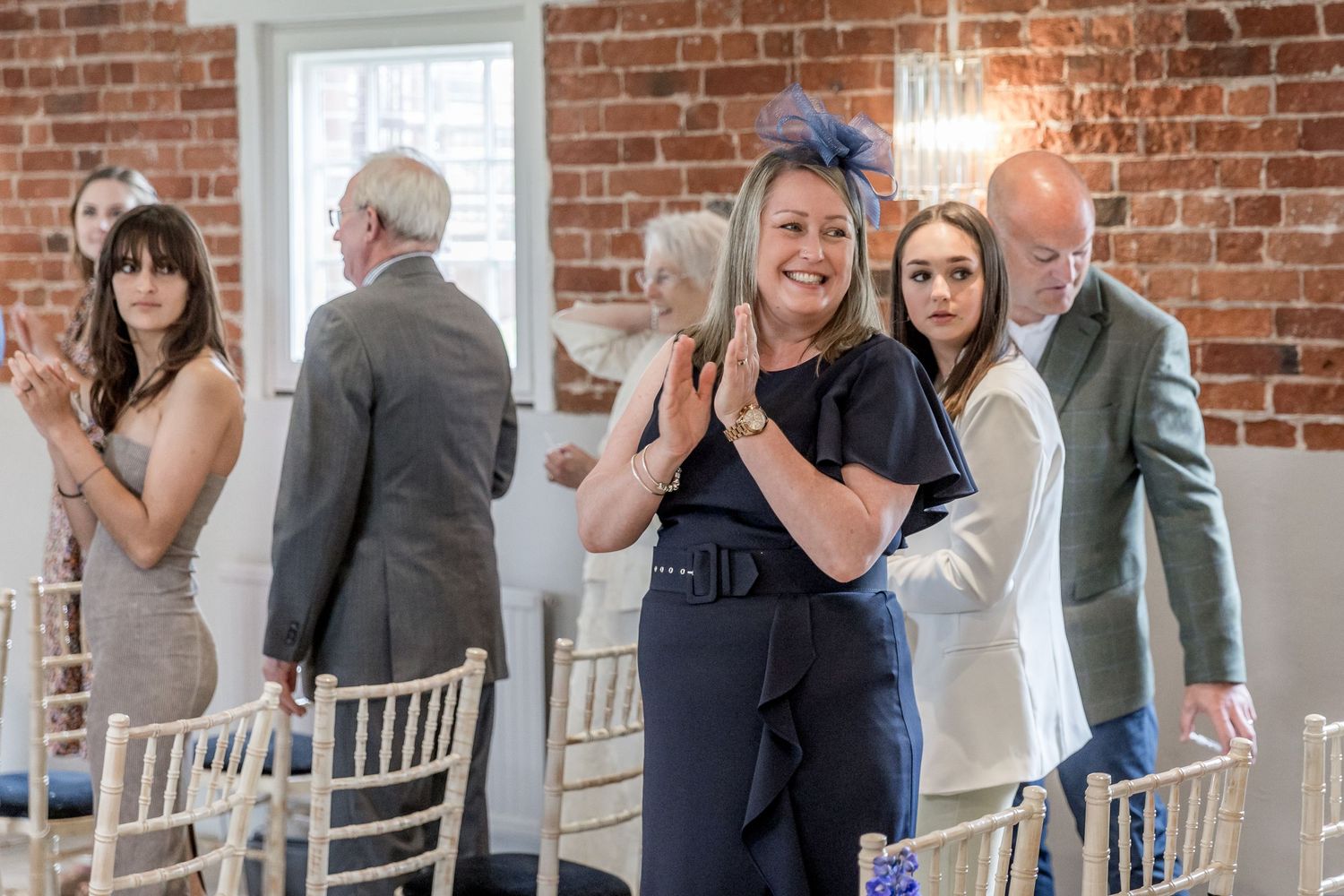 Wedding guests mingling in elegant brick-walled venue with natural lighting.