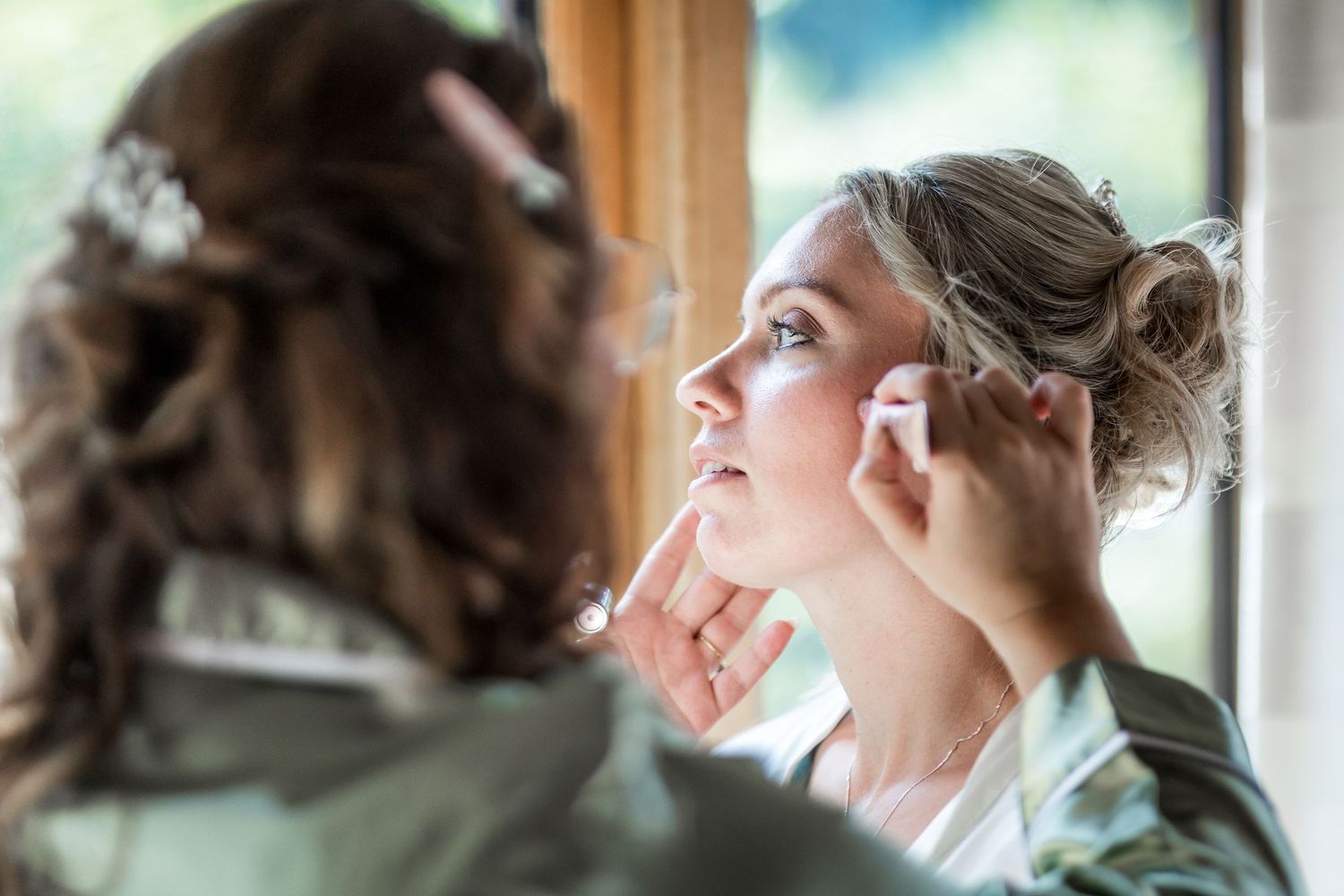 A person getting their makeup done while wearing a mint green robe before a special event.