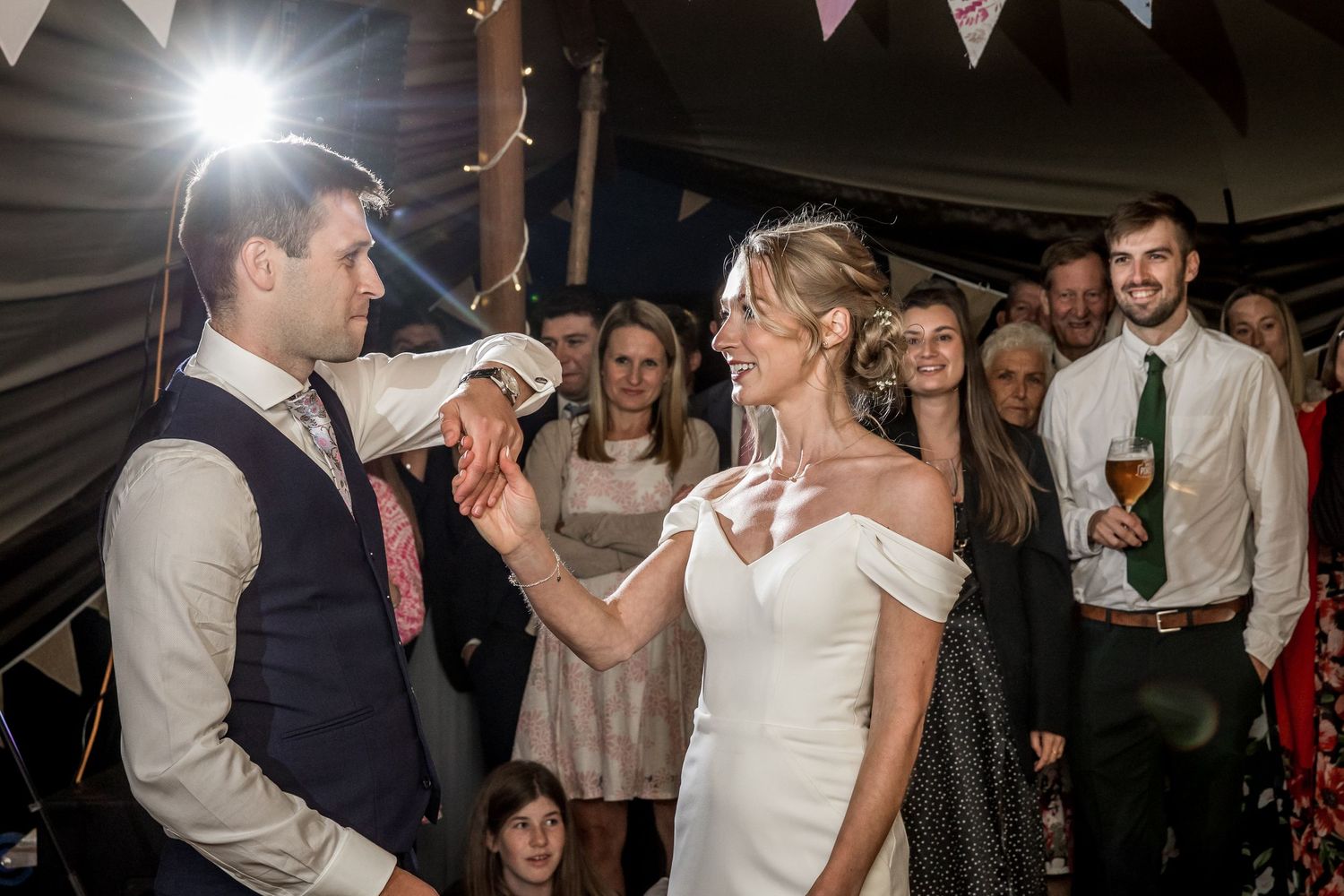 A couple shares drinks during their wedding reception under decorative bunting and lights.