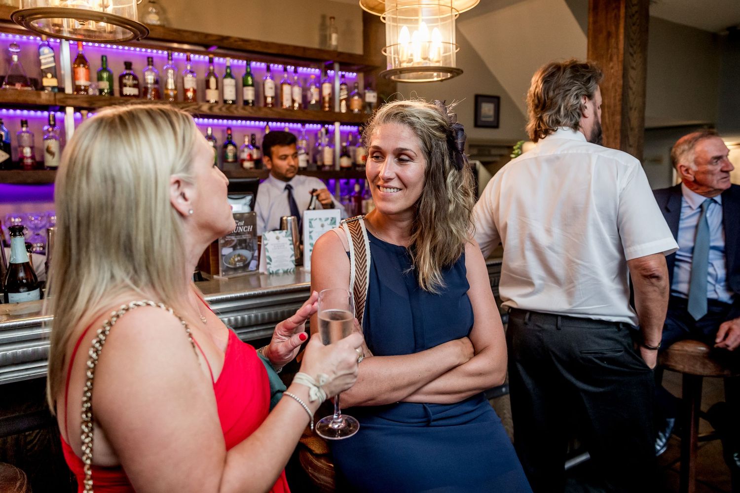 Wedding guests enjoying drinks and conversation at an elegant bar with purple lighting.