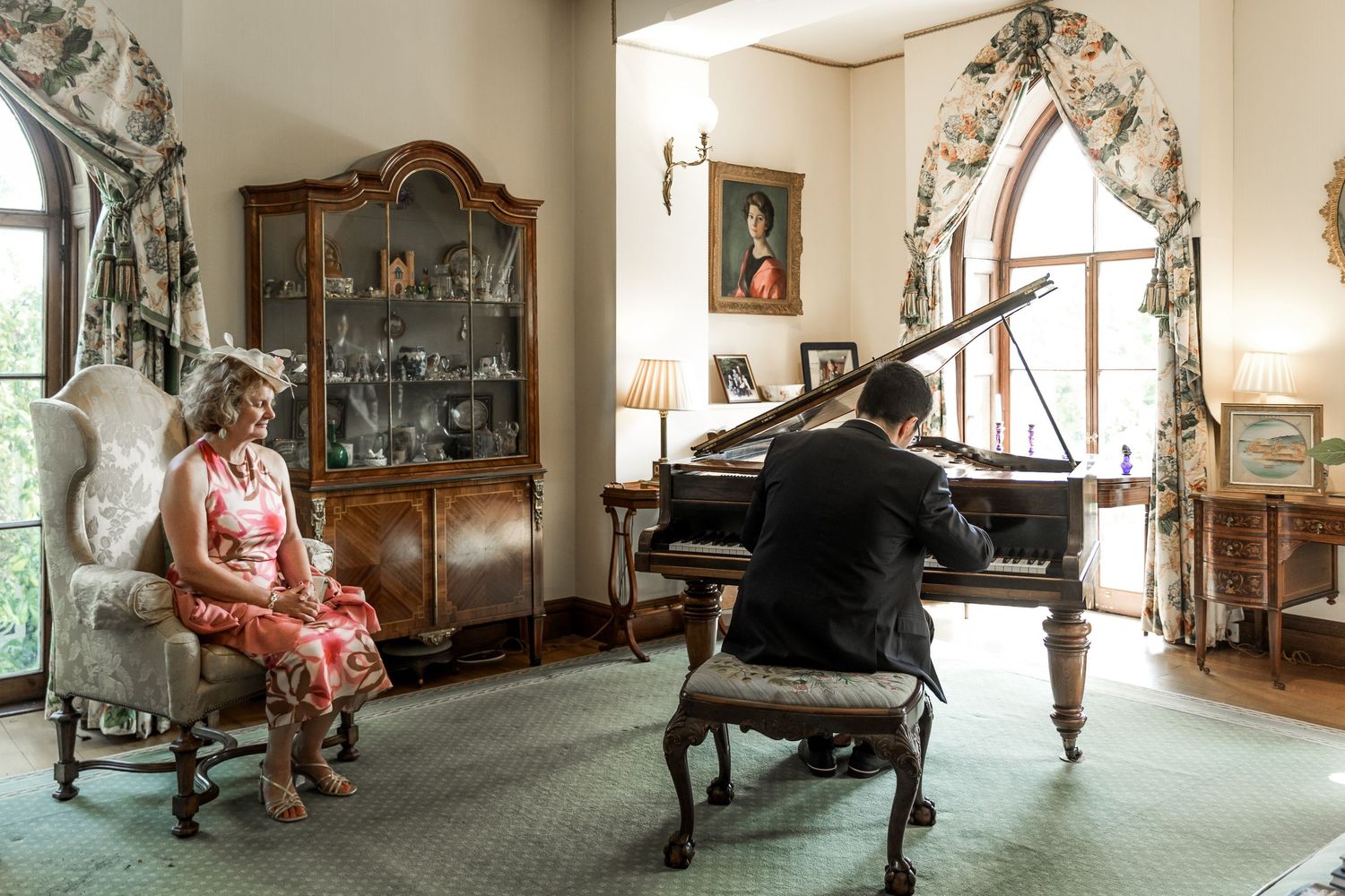 A wedding guest plays piano for the bride and groom in the elegant drawing room of Houghton Lodge, Hampshire wedding venue near Stockbridge