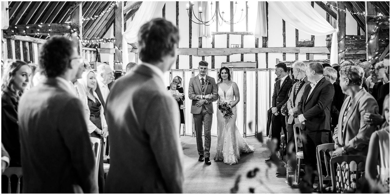 Black and white wedding photograph of the bride walking down the aisle at Clock Barn