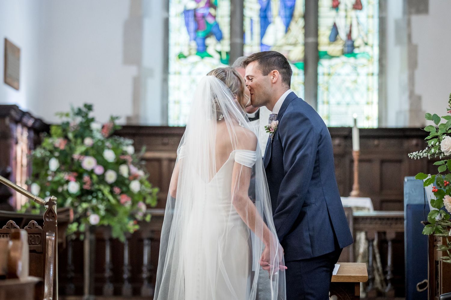 Wedding ceremony in church with stained glass windows and floral decorations.