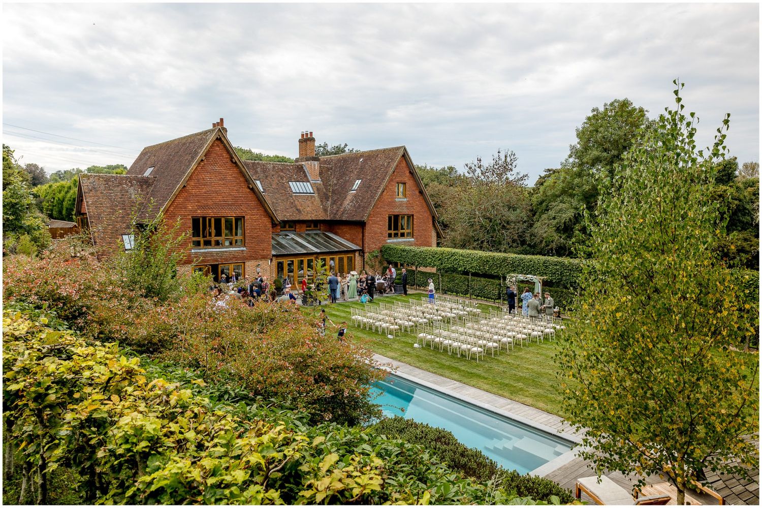 Panoramic view of a brick house with swimming pool and landscaped garden on a cloudy day.