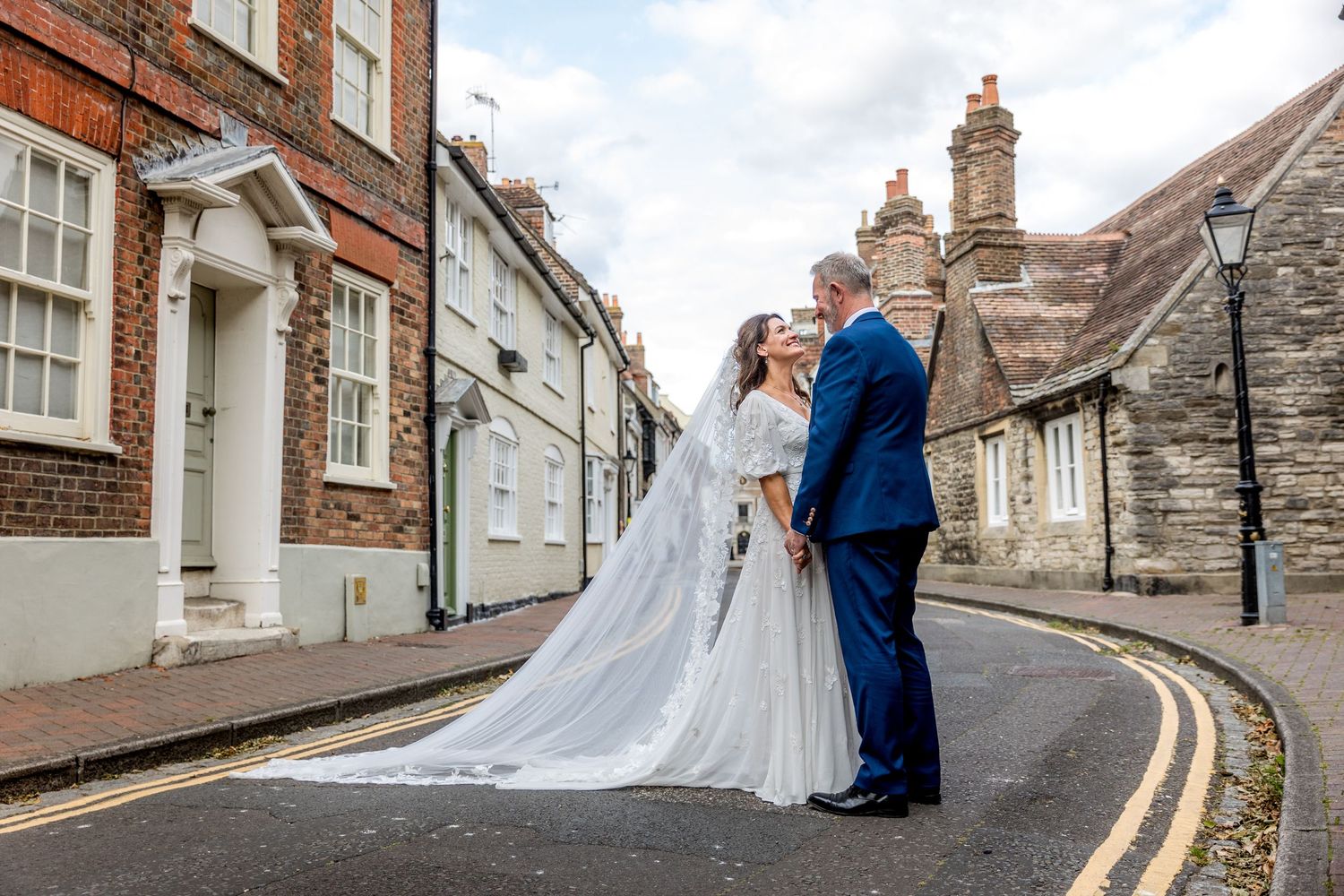 A wedding couple poses along a charming cobblestone street lined with historic brick buildings.