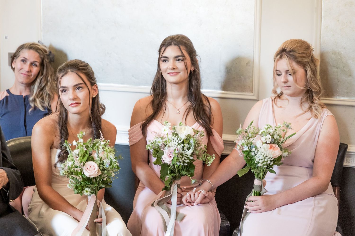Bridesmaids in pink dresses hold matching floral bouquets while seated.