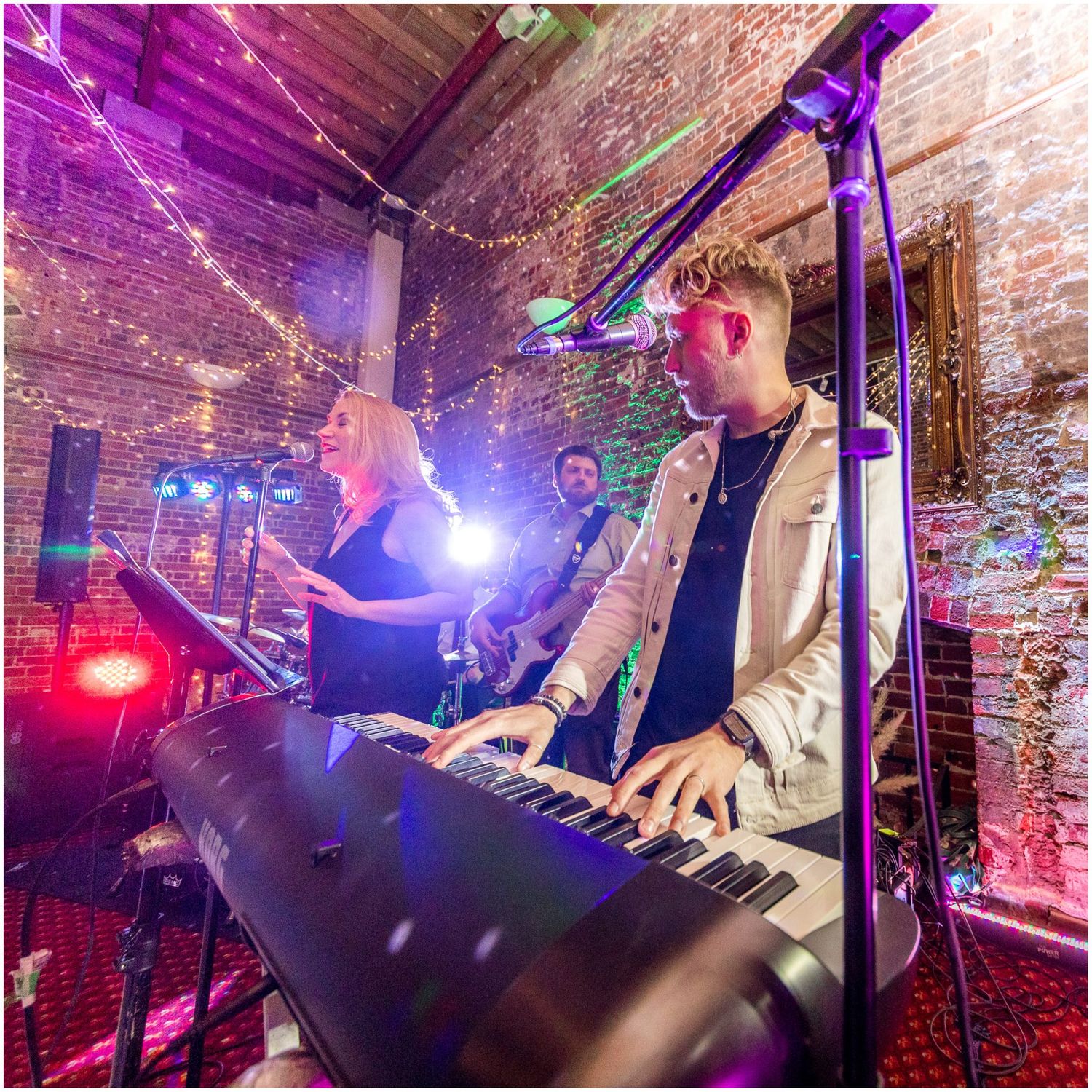Wedding band performs on stage with colorful purple and red lighting in a brick-walled venue.