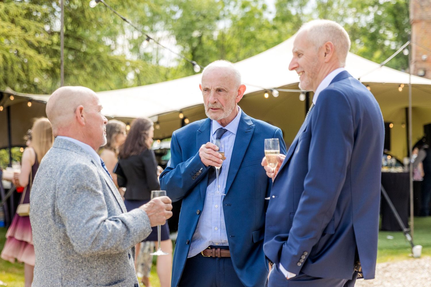Guests chatting and mingling during outdoor wedding reception under string lights.