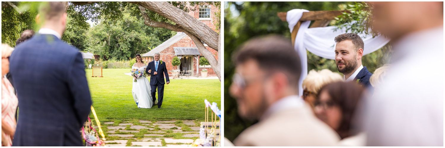 The groom watches as the bride walks across the lawn on her father's arm towards the outdoor ceremony area at Sopley Mill near Christchurch