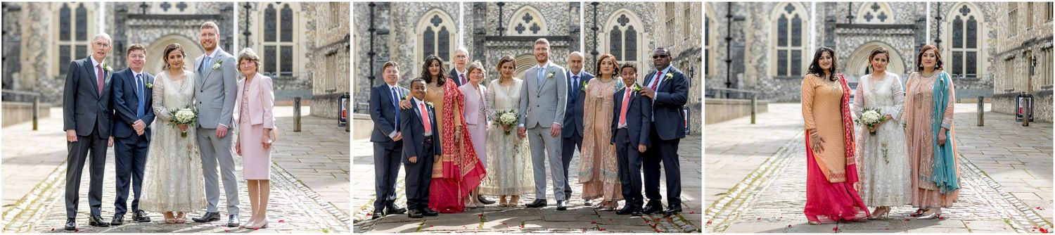 Wedding party and guests gathered outside historic stone building for photographs.