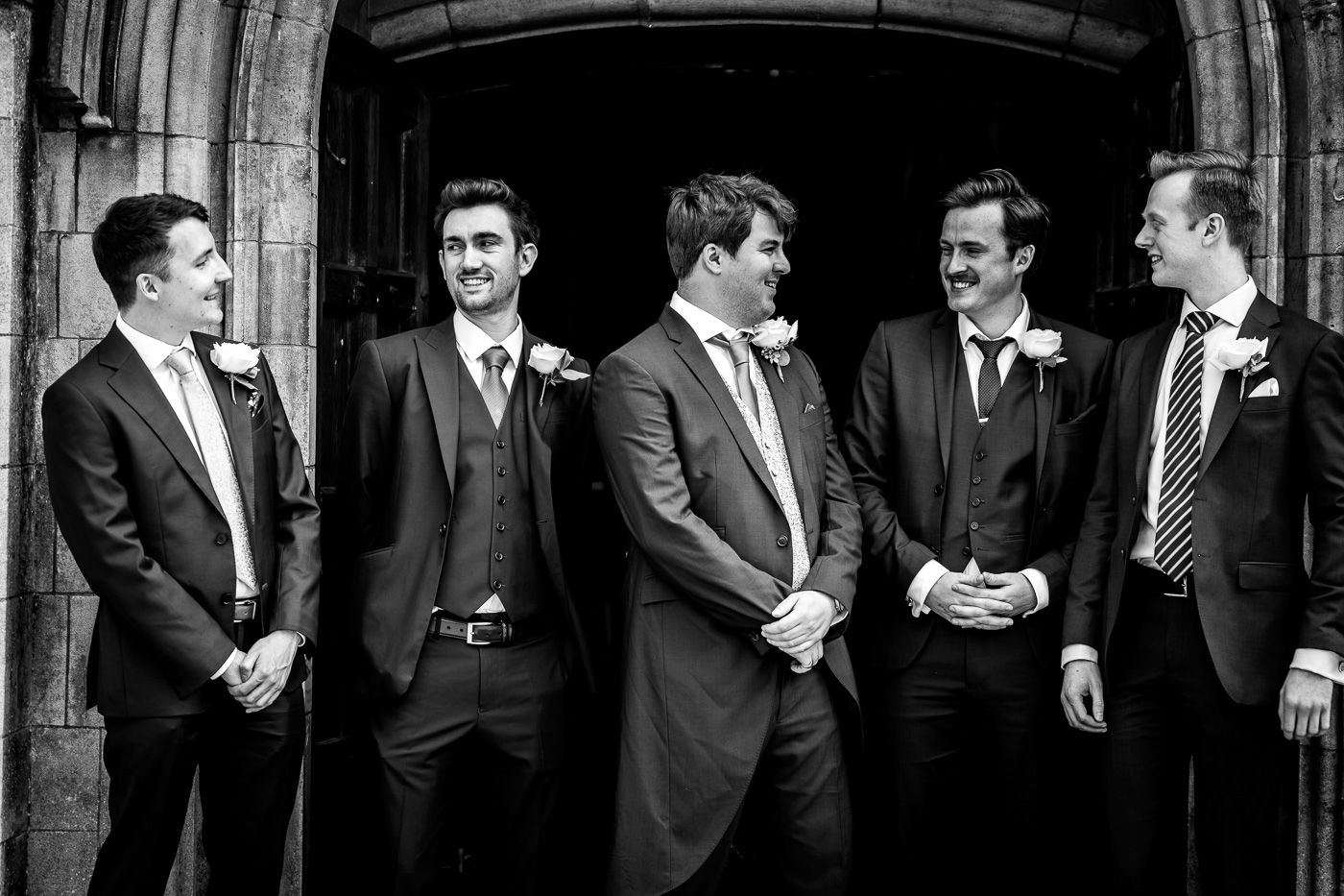 Groomsmen in formal attire laughing together in black and white photography.