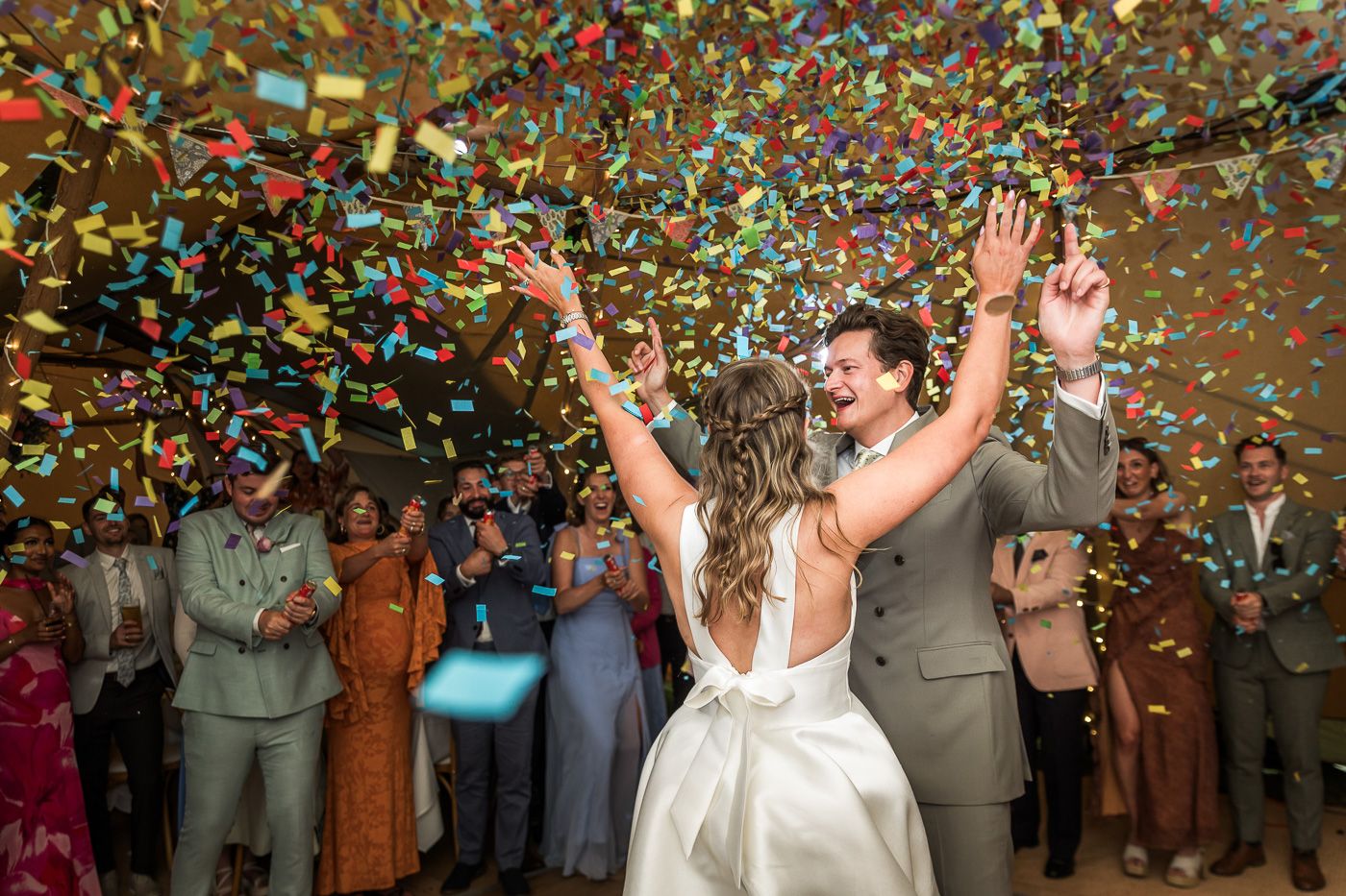 Joyful confetti celebration moment with wedding party and guests.