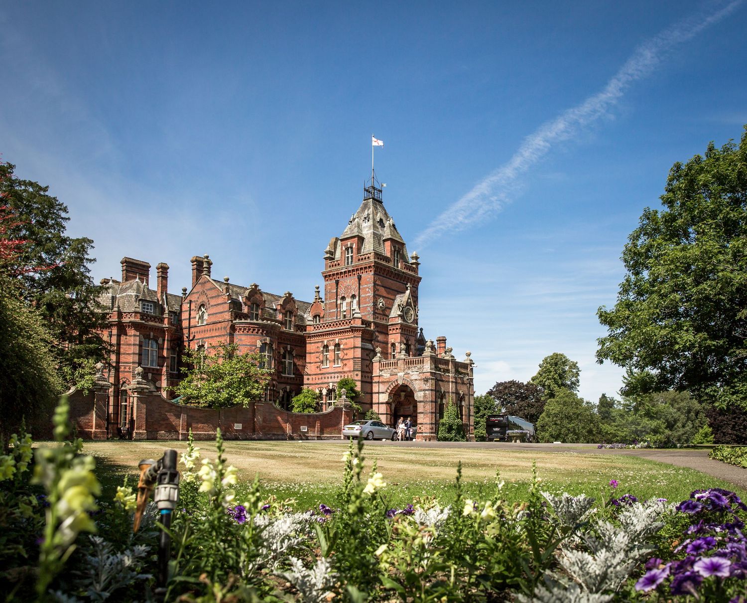 Panoramic view of a grand Victorian mansion with manicured gardens and blue summer sky.