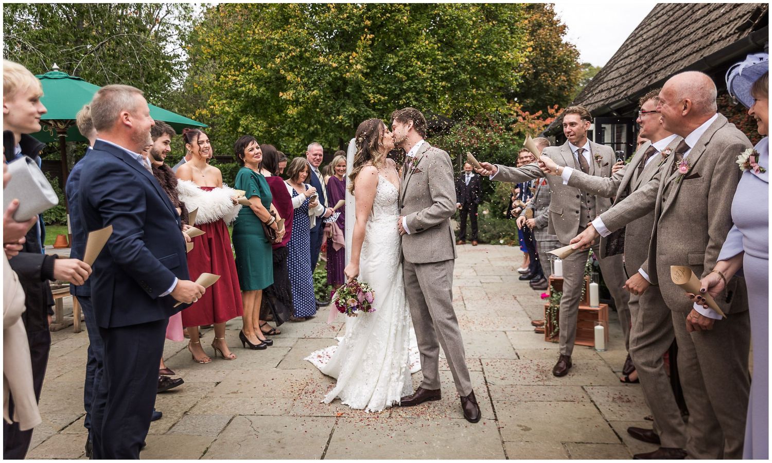 The bride and groom stop to kiss as they walk out between wedding guests who shower them with confetti at Clock Barn in Hampshire