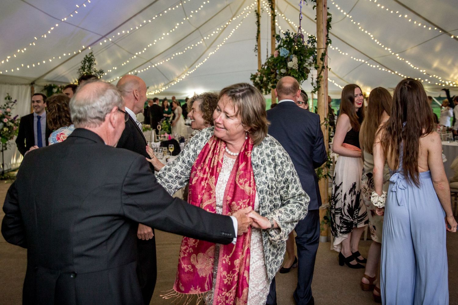 Wedding guests dancing and celebrating under tent with string lights.
