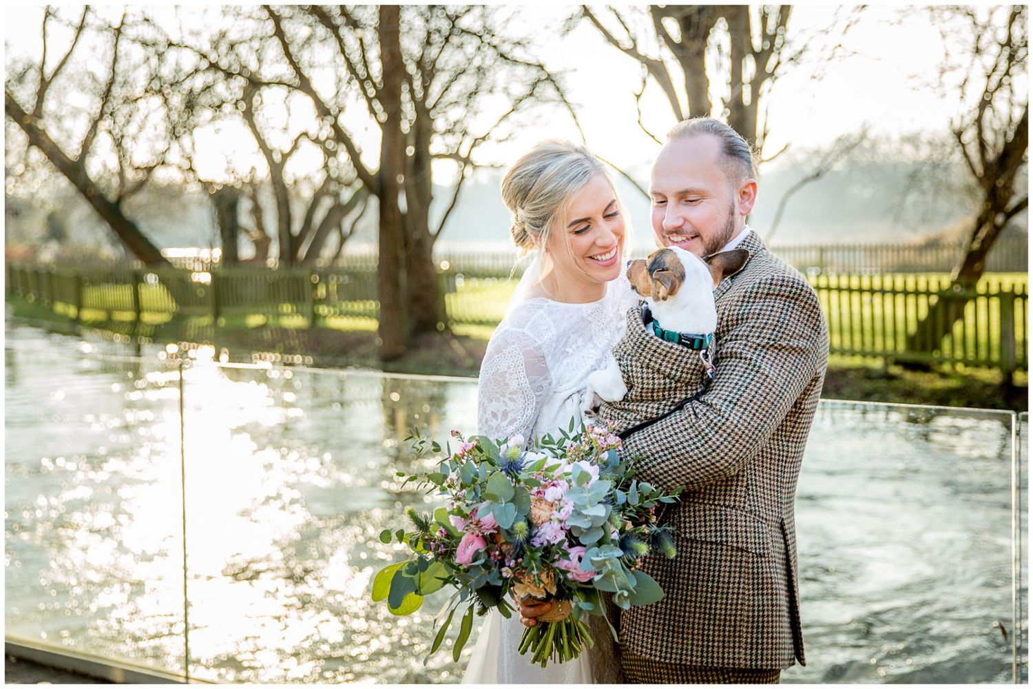 Romantic wedding photos captured by a lake with bare trees and reflective water.