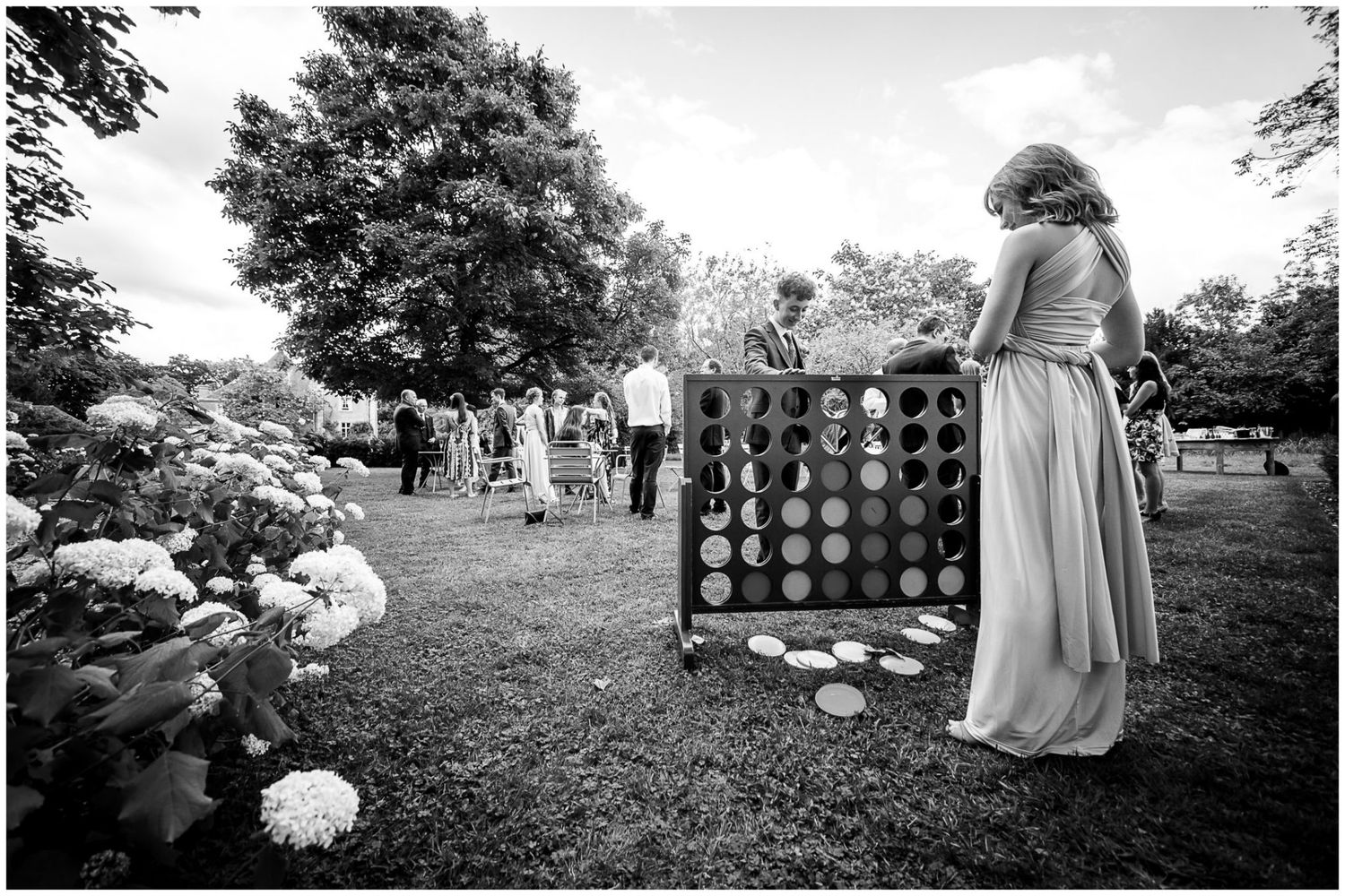 Black and white panoramic view of a wedding ceremony setup outdoors with chairs and decorative elements in a garden setting.