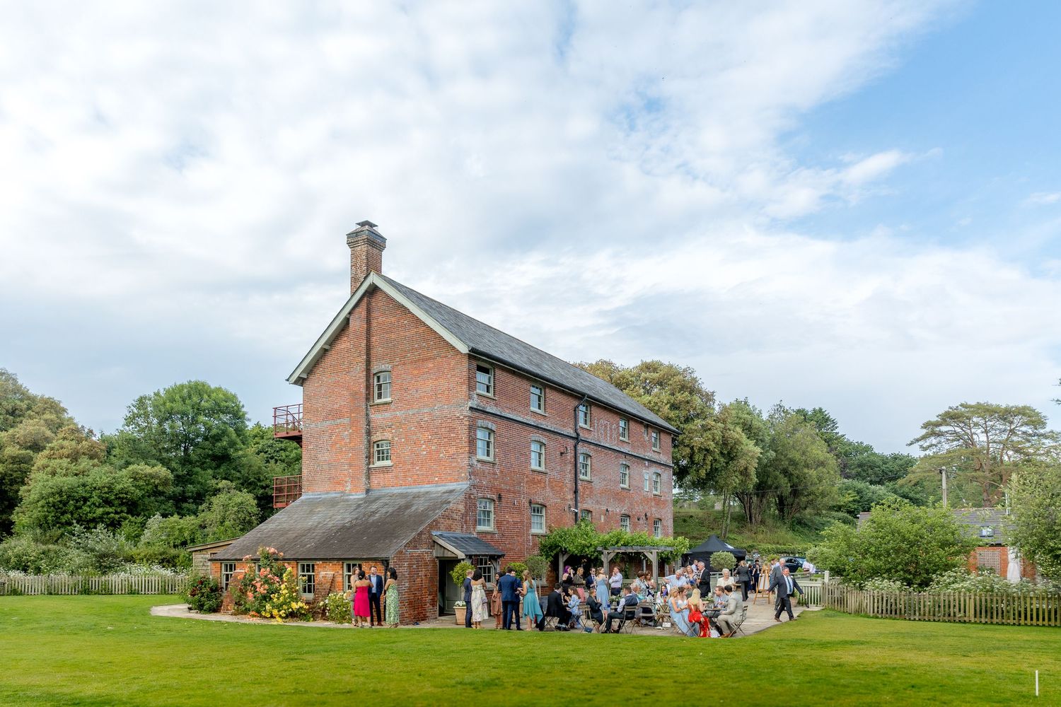 Panoramic view of a rustic brick venue with guests gathering outside on a sunny day.