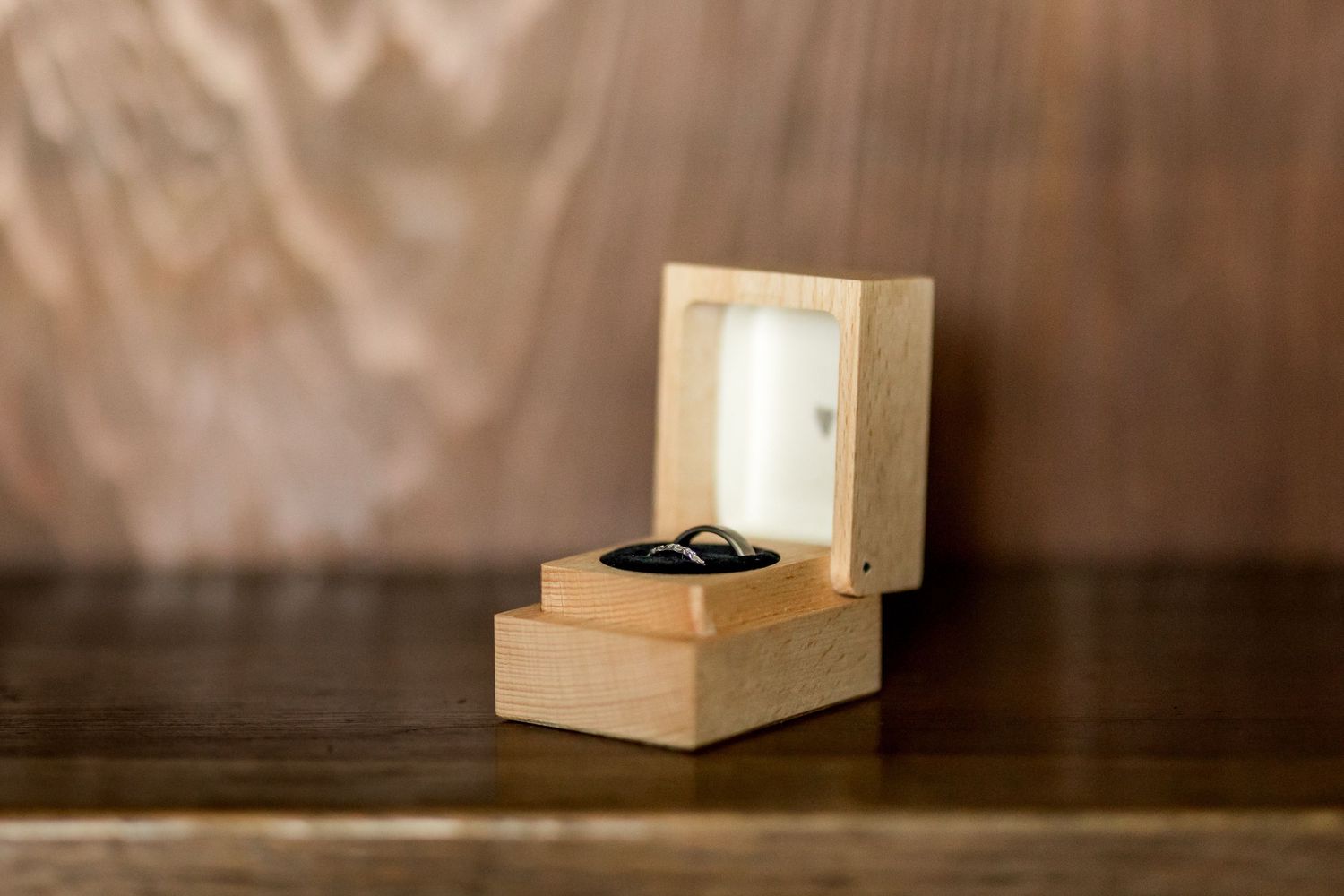 Small wooden box containing jewelry sitting on dark wooden surface.