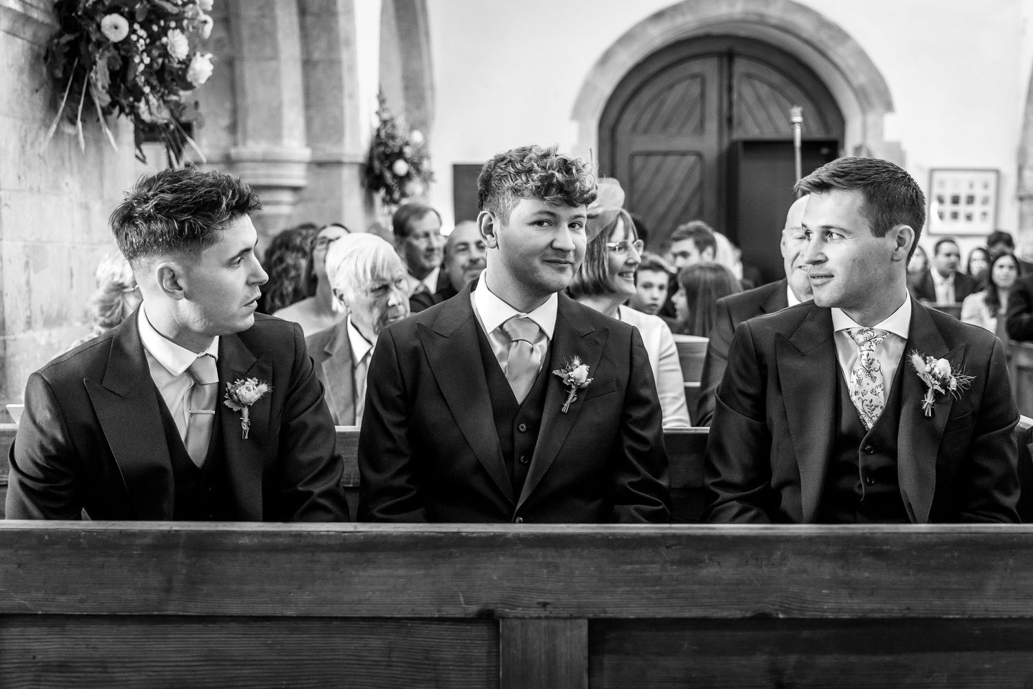Groomsmen seated in church pews during a traditional wedding ceremony.