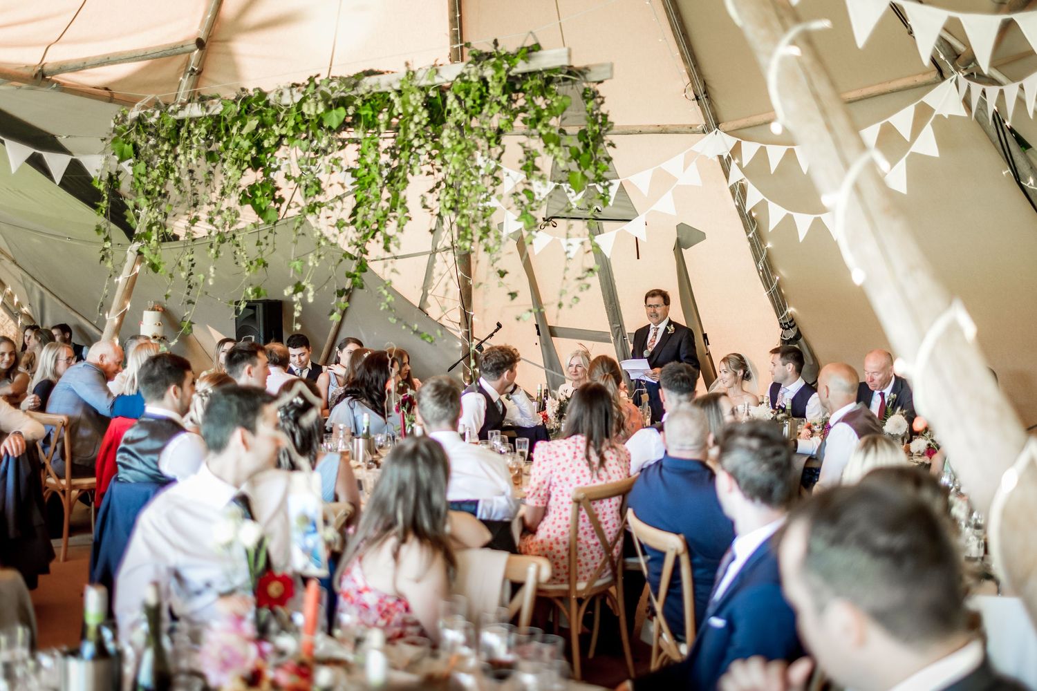 Elegant wedding reception setup in a marquee tent with floral decorations and white bunting.