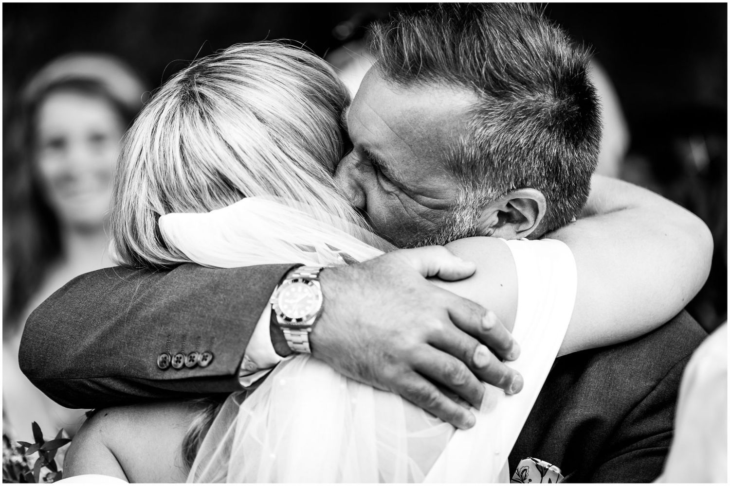Black and white photograph of the bride receiving a hug from a wedding guests following her marriage ceremony