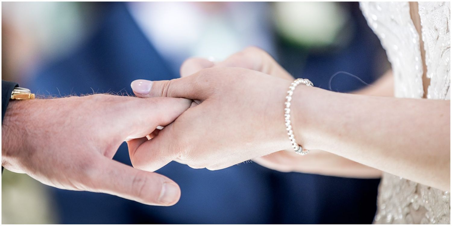 Close up of wedding ring exchange during indoor ceremony.