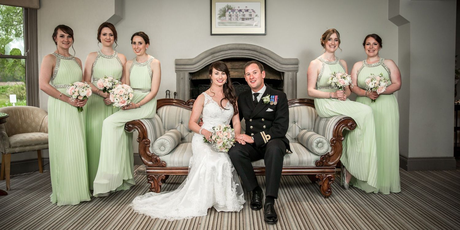 Wedding group photograph with bride, groom and bridesmaids taken indoors by the fireplace at Southdown Manor in Hampshire.
