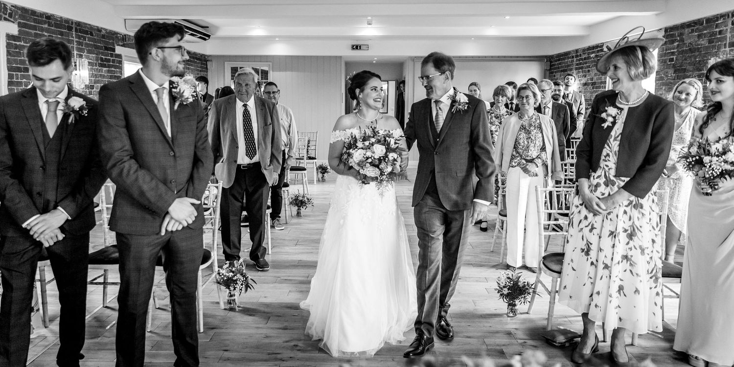 Wedding guests stand in line during a ceremony in an elegant indoor venue with brick walls and hardwood floors.