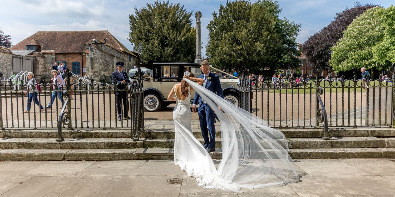 Outdoor wedding scene with stone buildings and green trees in the background.
