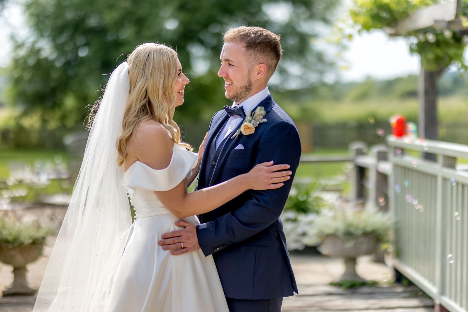 A bride and groom share an intimate moment together on their wedding day in a sunny outdoor garden setting.