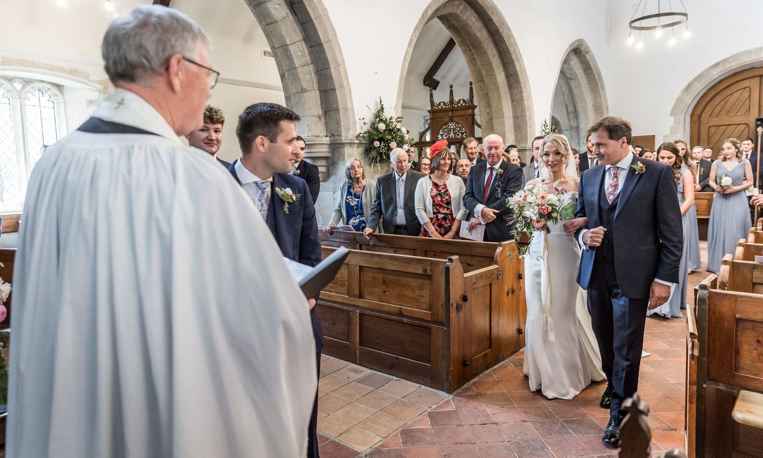 Wedding guests gather in church pews during a traditional ceremony beneath ornate arches and chandeliers.