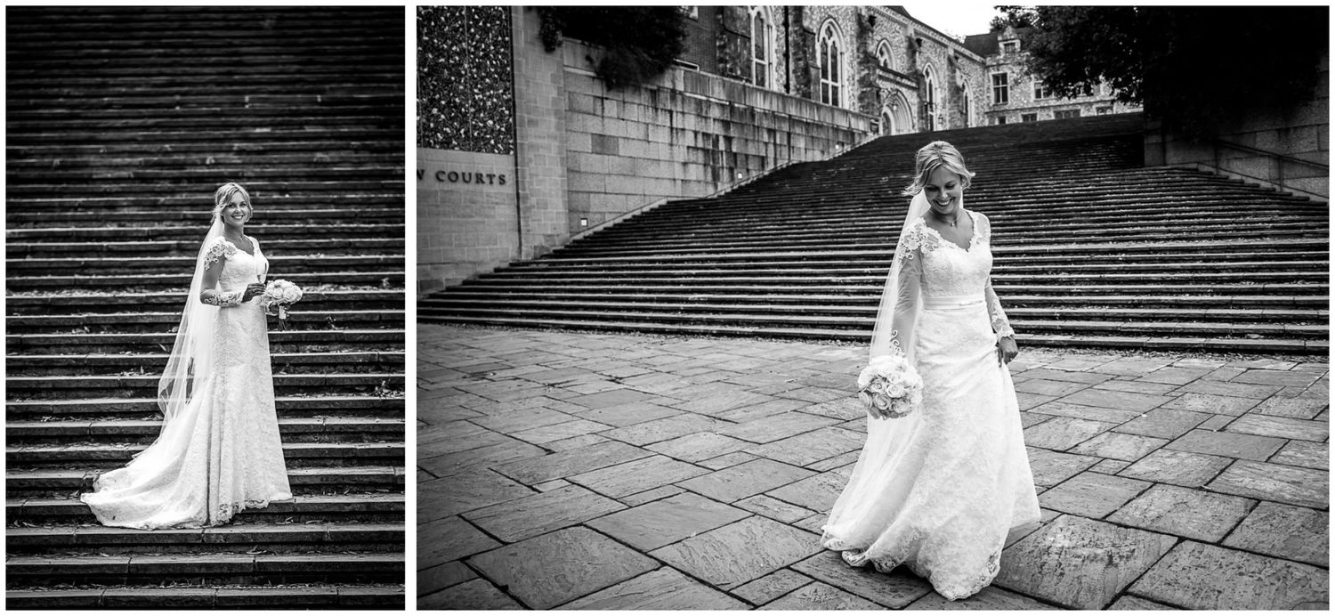 A bride in a flowing white gown poses gracefully on grand stone steps in a black and white photograph.